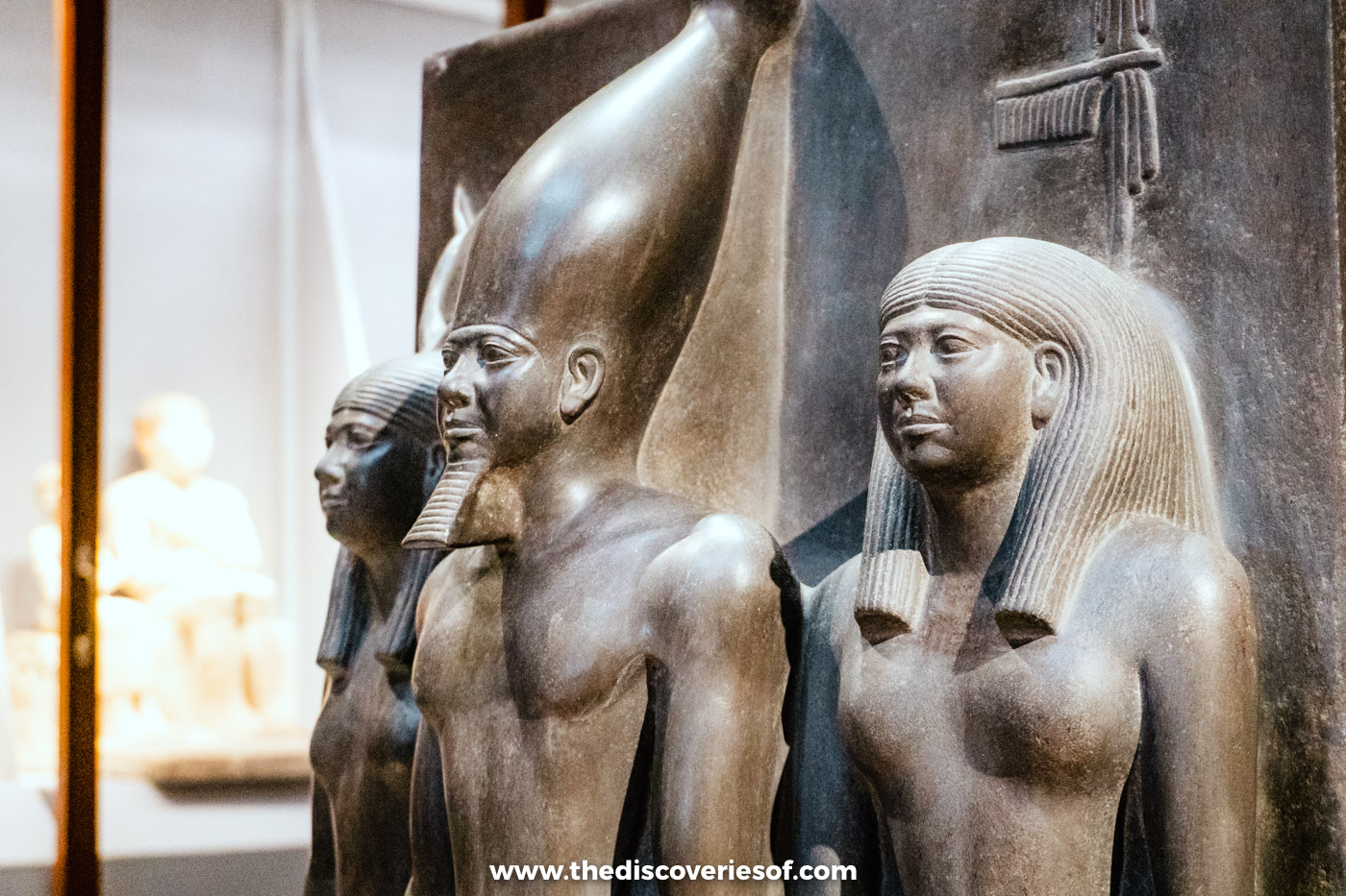 A dark stone triad statue of King Menkaure standing between two goddesses in the Egyptian Museum in Cairo