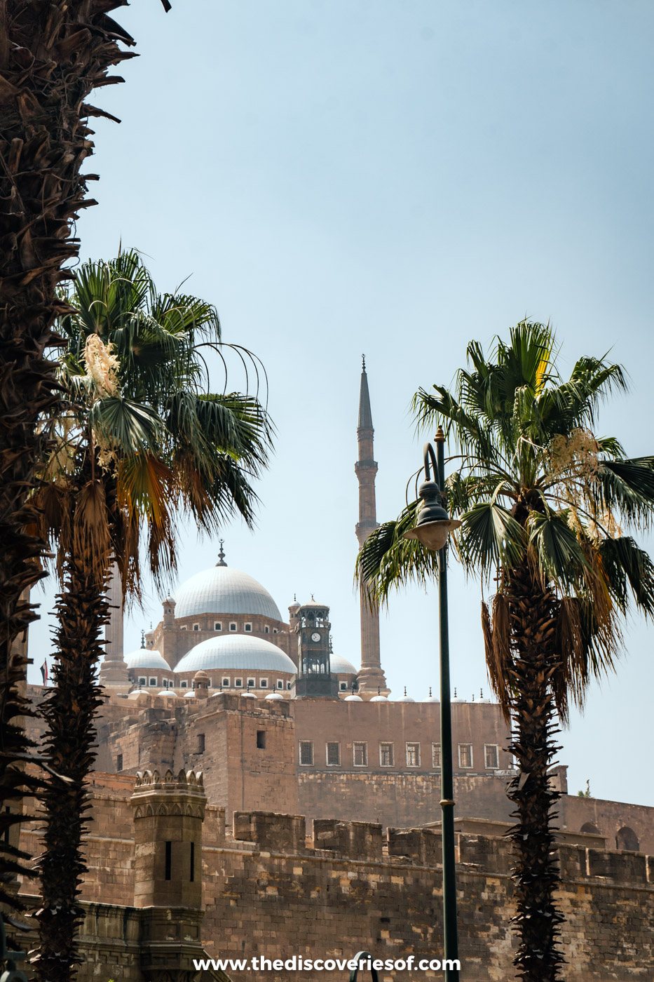 The domes and twin minarets of the Mosque of Muhammad Ali rising above the Cairo Citadel walls and palm trees