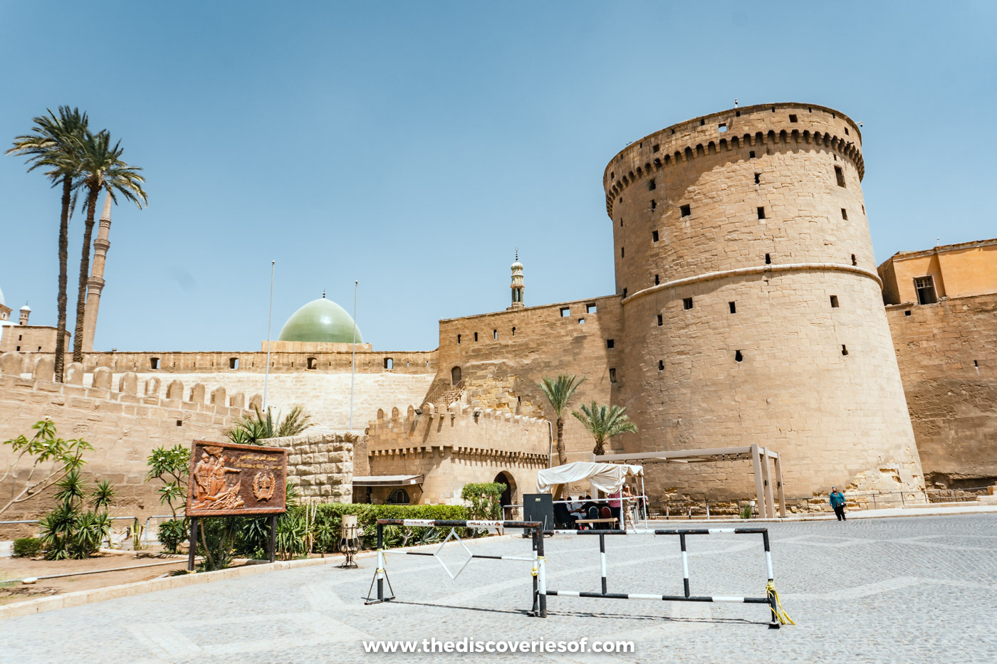A round stone tower of the Cairo Citadel with the green dome of the Mosque of al-Nasir Muhammad behind