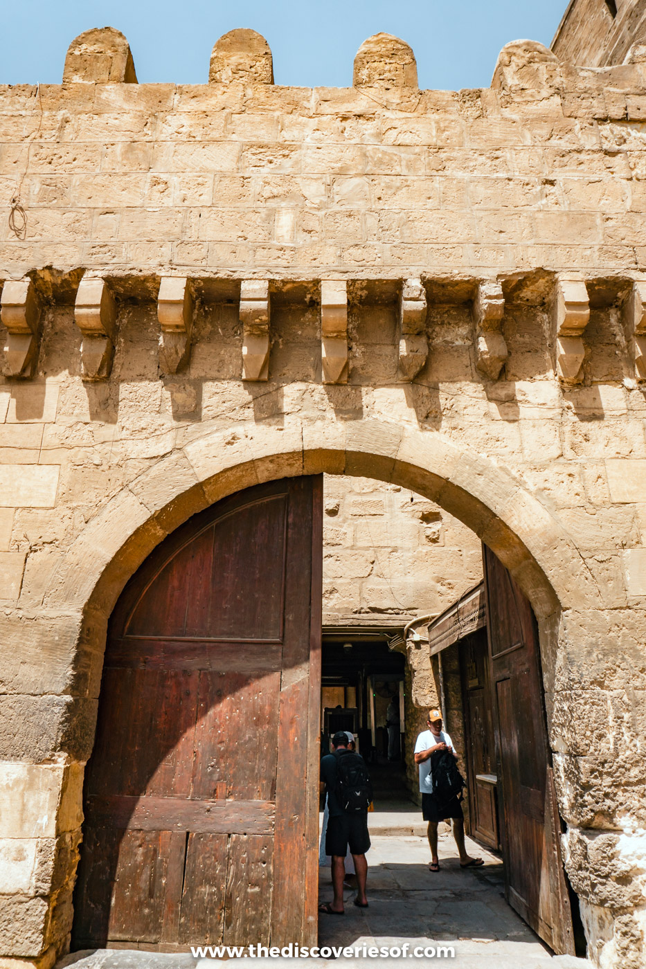 A crenellated stone gateway with open wooden doors leading into the Cairo Citadel