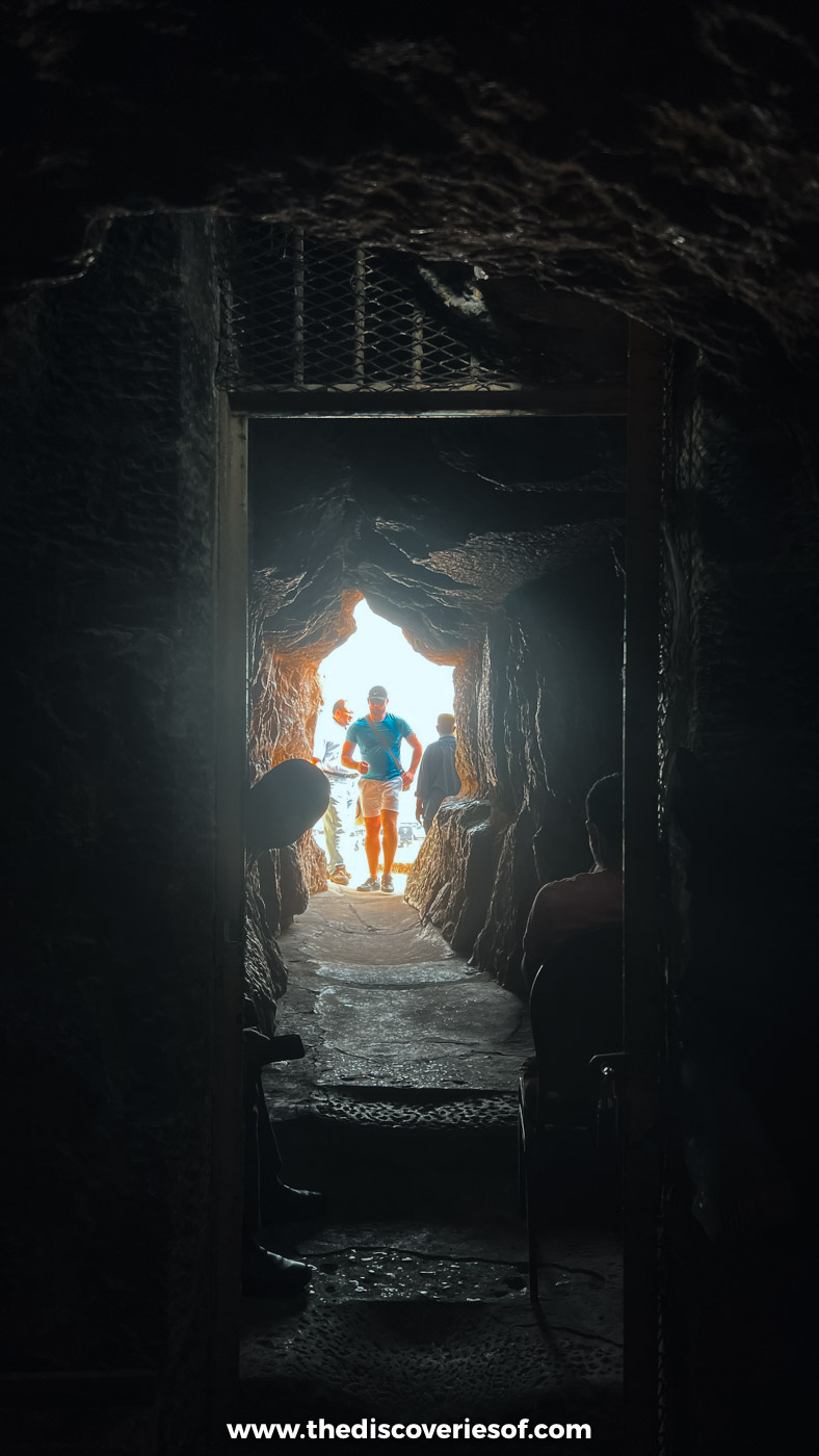 A dark stone passage inside the Great Pyramid of Giza opening onto bright daylight and visitors at the entrance