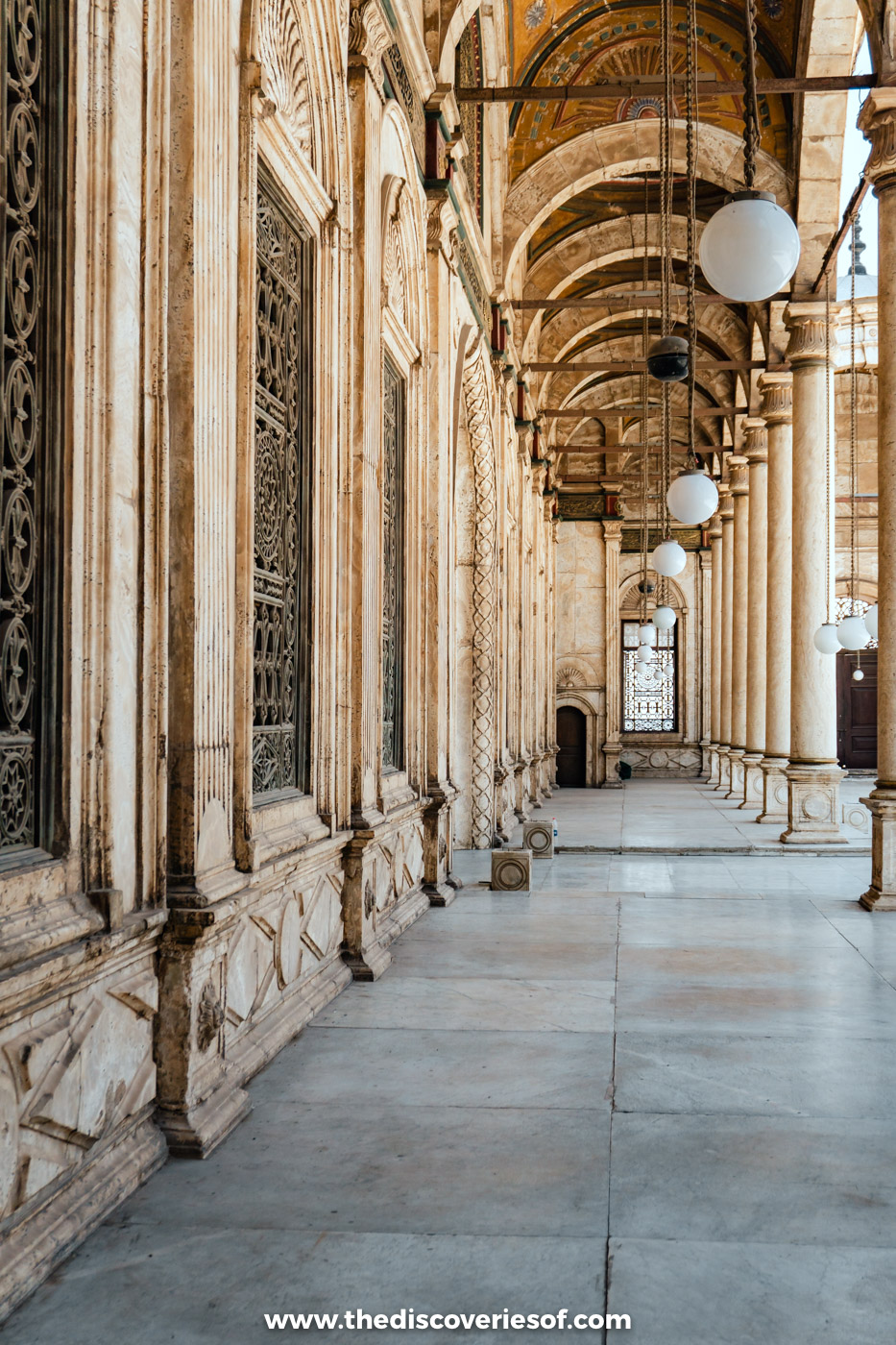 A long marble arcade with hanging globe lamps along the courtyard of the Mosque of Muhammad Ali