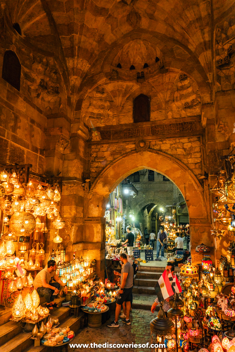 Glowing brass lanterns hanging in shops under a stone arch in the Khan el-Khalili bazaar in Cairo