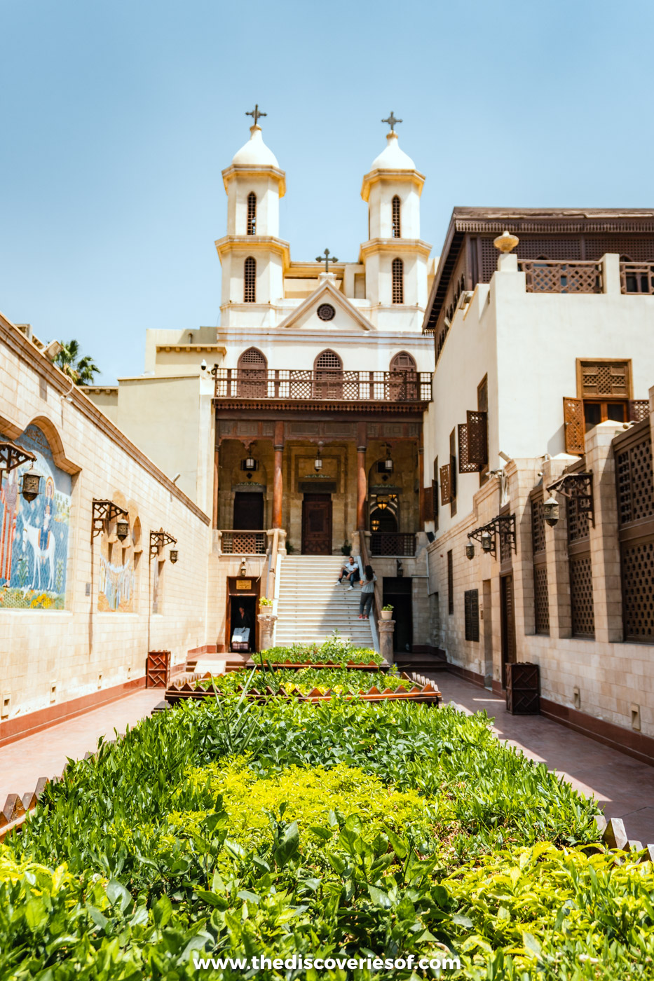 The twin bell towers of the Hanging Church rising above a green garden courtyard in Coptic Cairo
