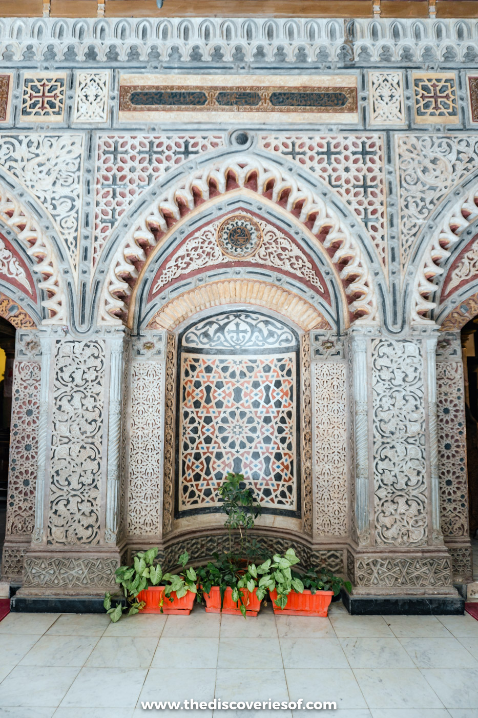 The intricately carved arched facade of the Hanging Church in Coptic Cairo, with potted plants at its base