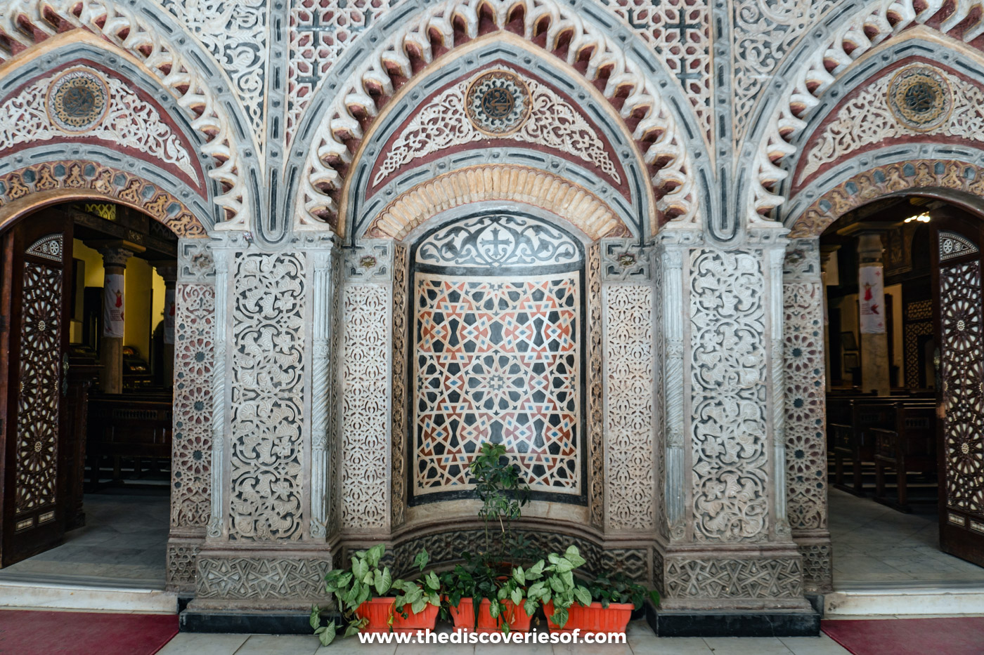 The ornately carved arched facade and doorways of the Hanging Church in Coptic Cairo, with potted plants