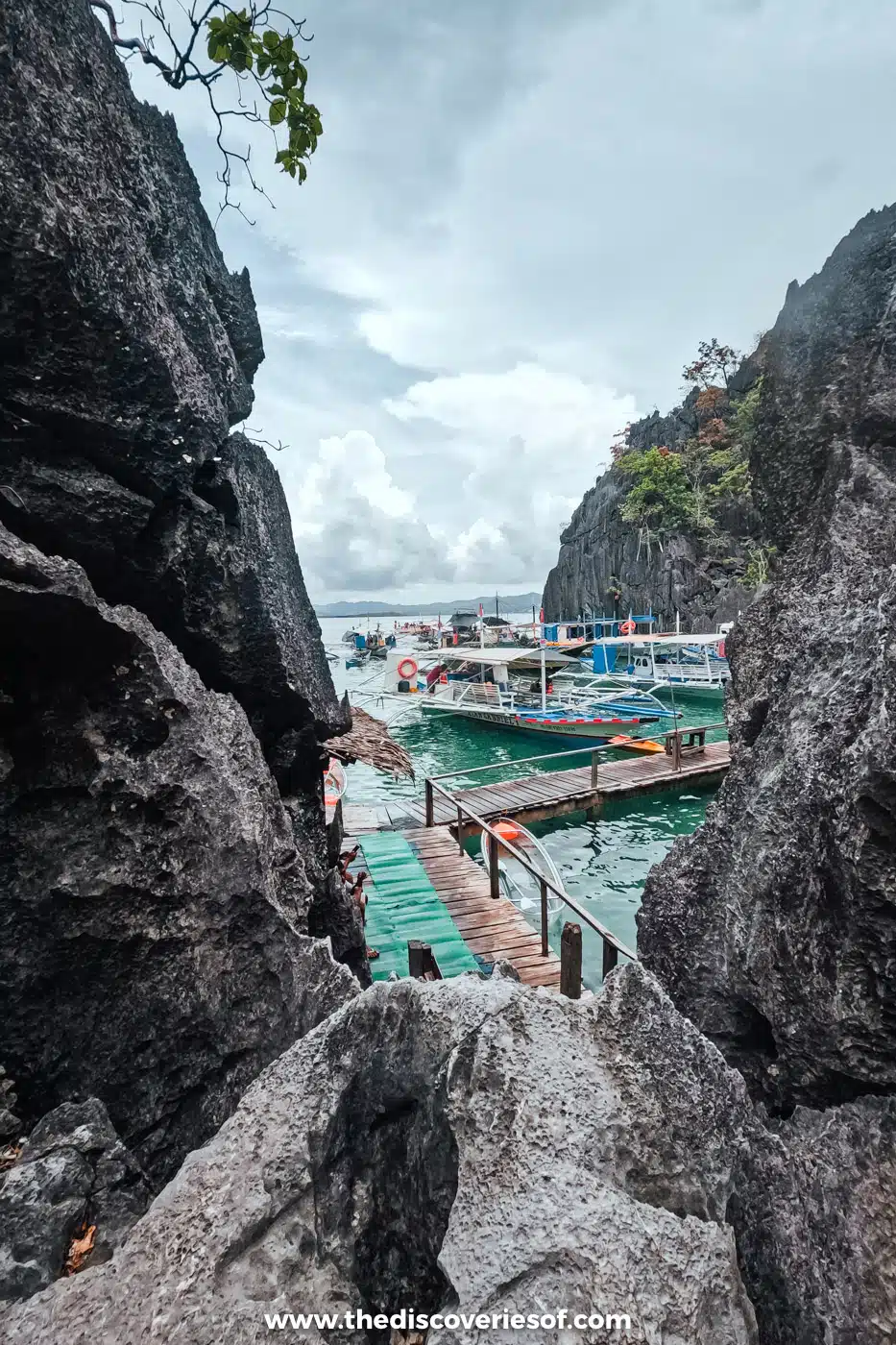 Wooden walkway winding between jagged limestone rocks down to moored boats on Coron Island