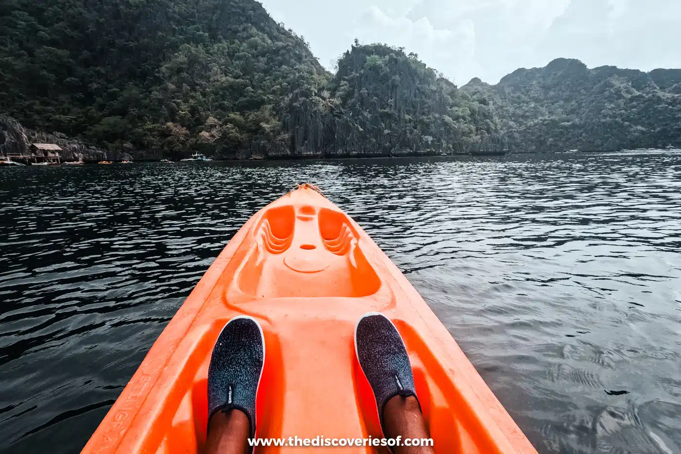 Orange kayak on the still water of the inner Twin Lagoon below forested limestone cliffs, Coron