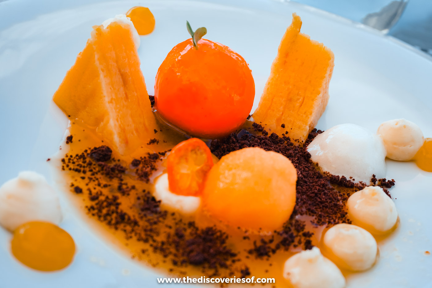 A plated dessert of orange spheres, sponge and crumble on a white plate at DOC restaurant in the Douro Valley