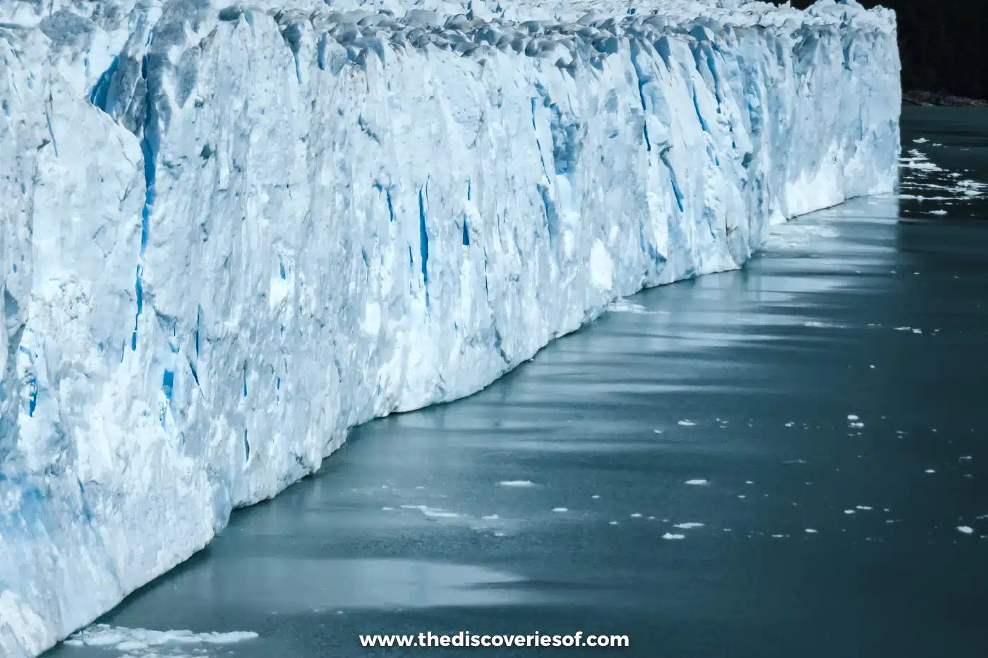 Sheer blue ice wall of the Perito Moreno Glacier rising from the dark lake, Argentina