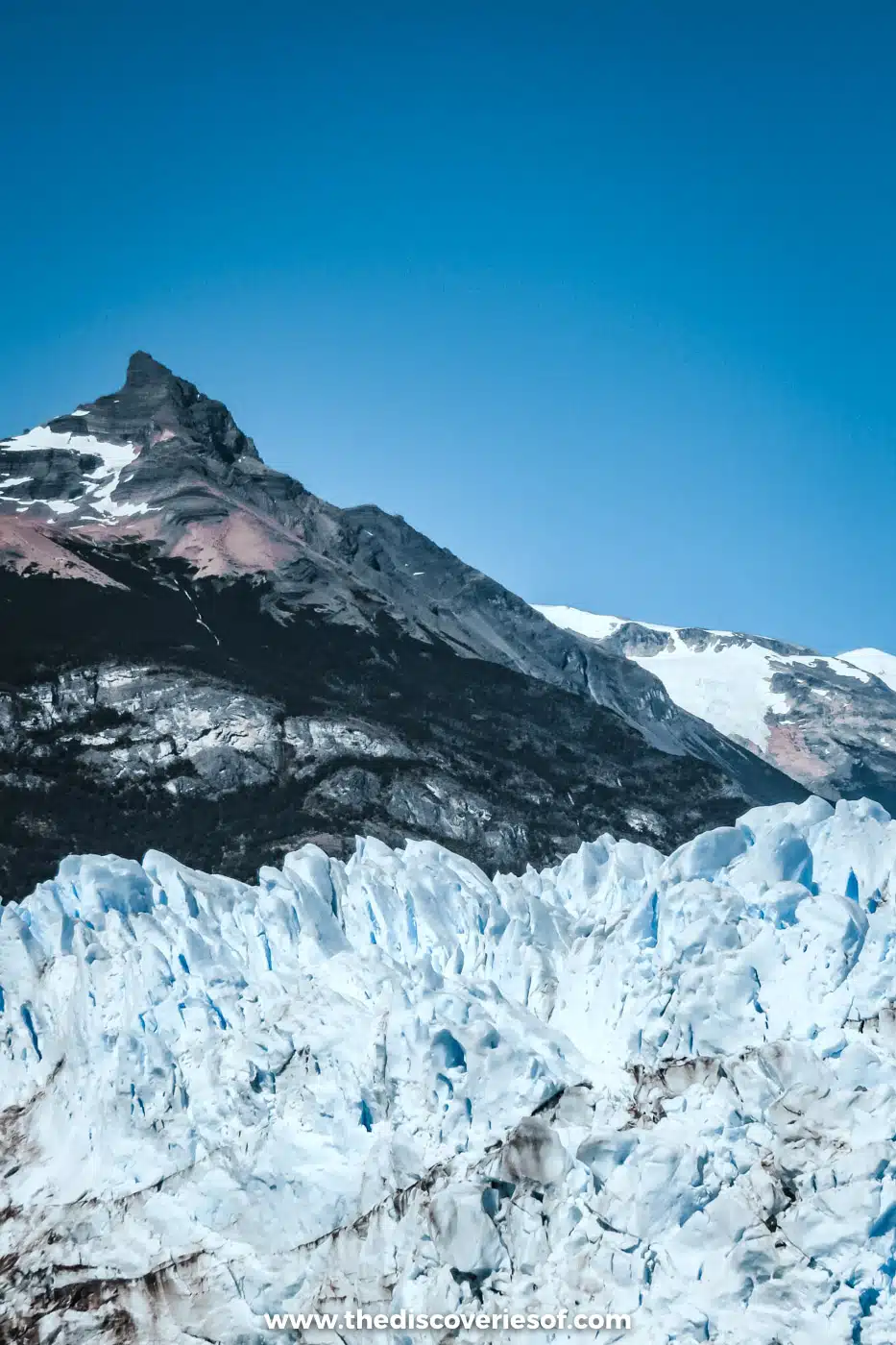 Jagged ice of the Perito Moreno Glacier beneath a rocky peak and a clear blue sky, Argentina
