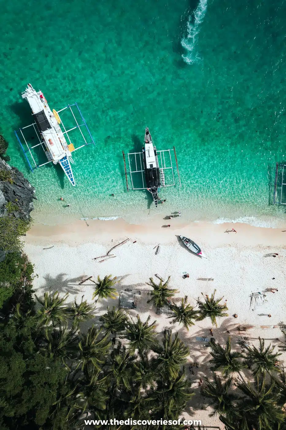 Aerial view of bangka boats moored off a palm-lined white-sand beach at Seven Commandos Beach, El Nido
