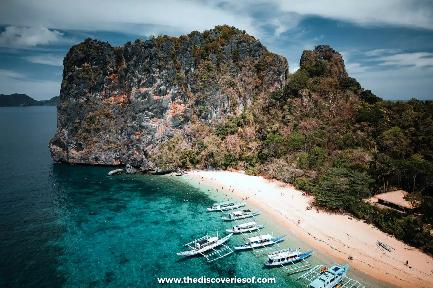 Aerial view of Helicopter Island's limestone rock and white beach with bangka boats moored offshore, El Nido