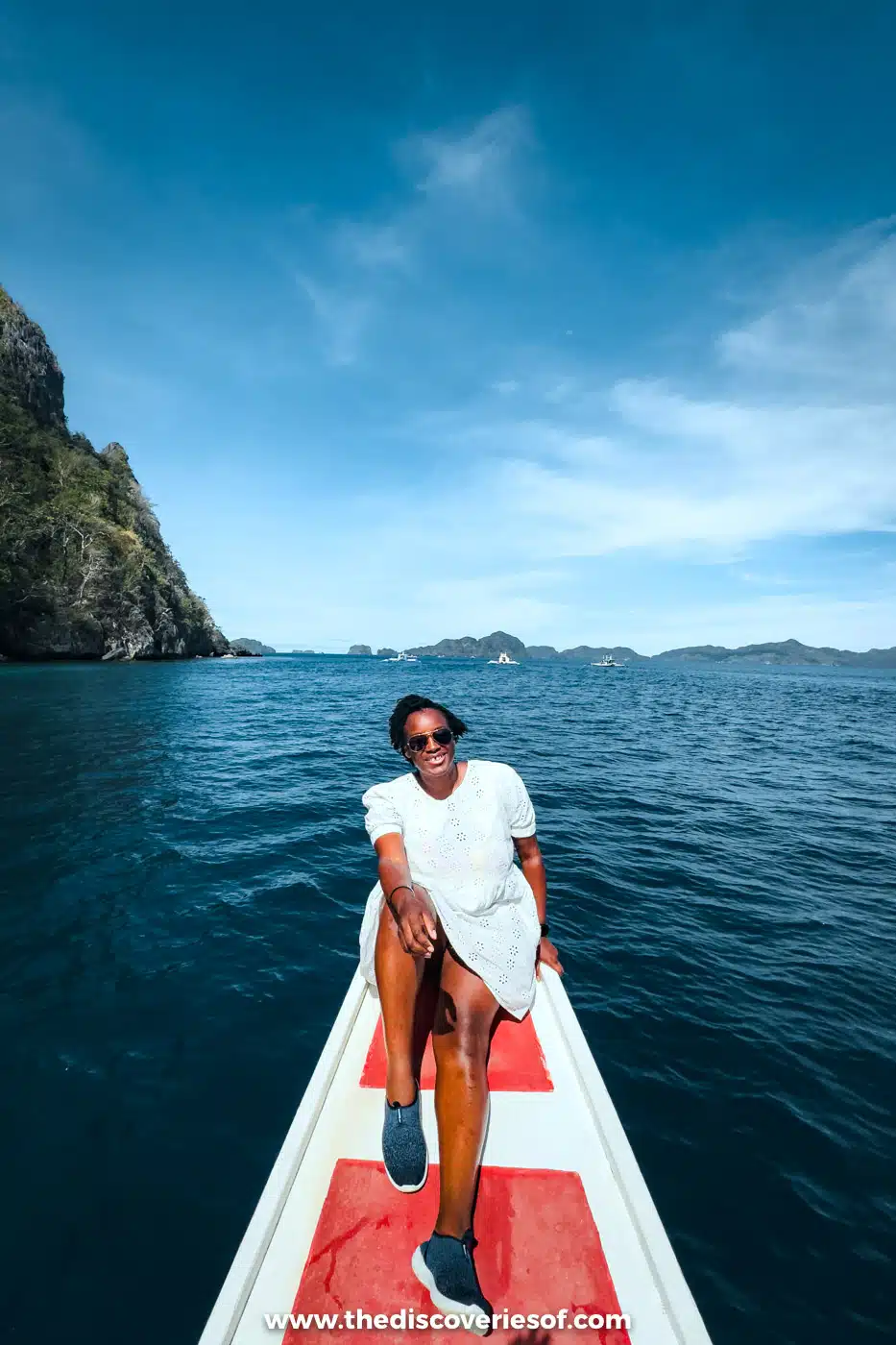 Julianna sitting on the bow of a bangka boat crossing Bacuit Bay towards limestone islands, El Nido