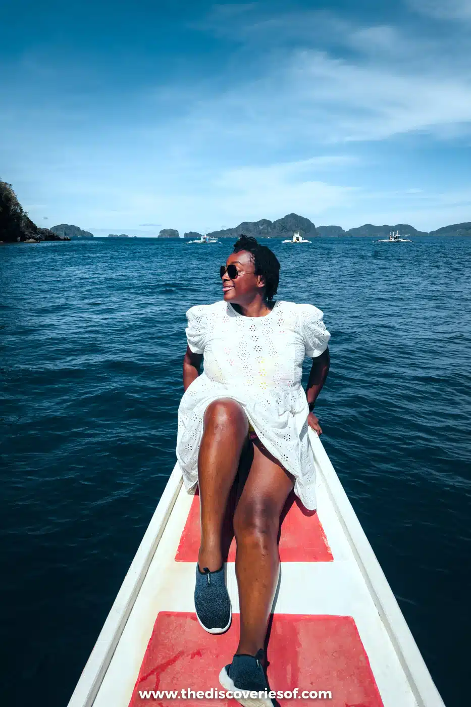 Julianna in a white dress sitting on the red and white bow of a bangka on the open sea, El Nido