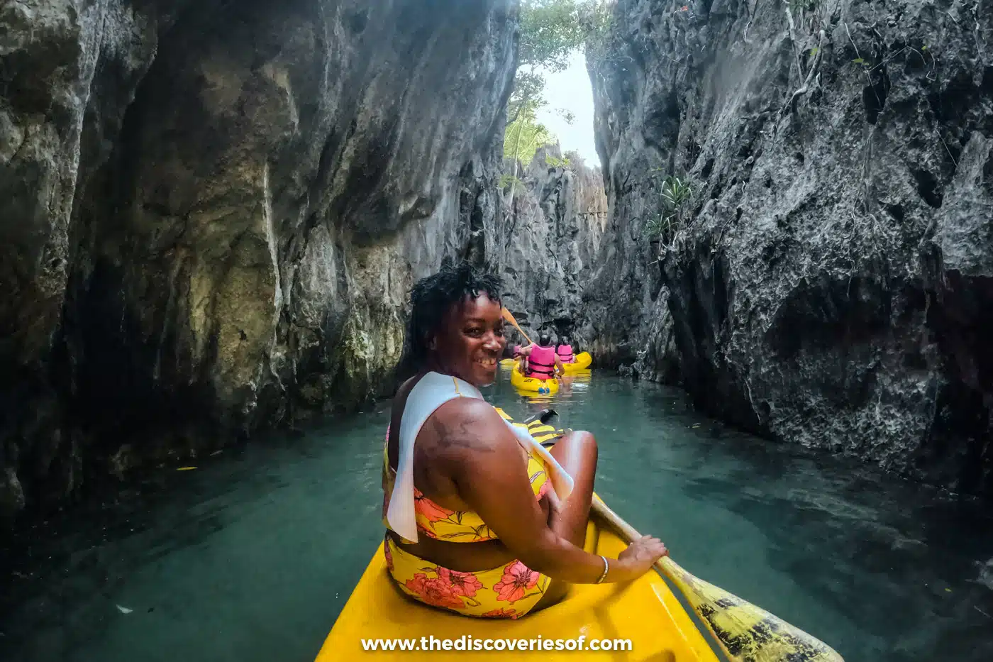 Julianna in a yellow kayak in a narrow channel between grey limestone walls in the Big Lagoon, El Nido