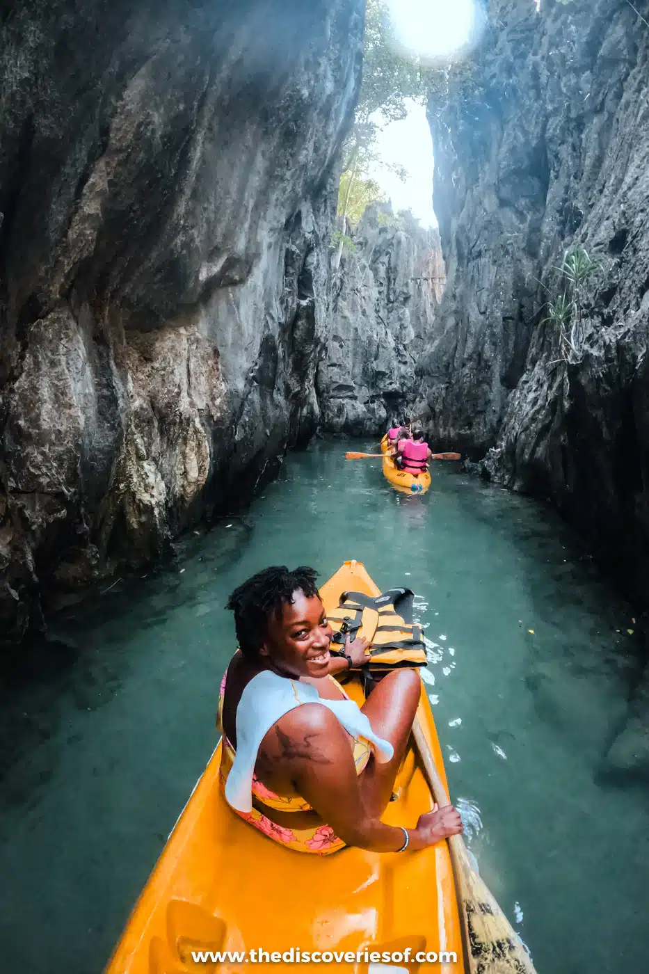 Julianna in a yellow kayak between towering grey limestone walls in a narrow lagoon on El Nido Tour A