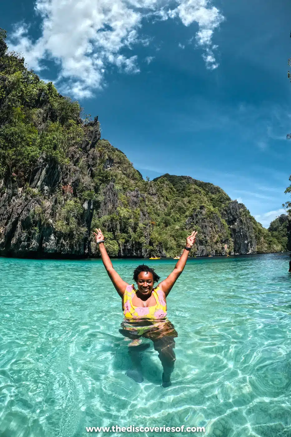 Julianna raising her arms in a turquoise lagoon ringed by limestone cliffs on El Nido Tour A
