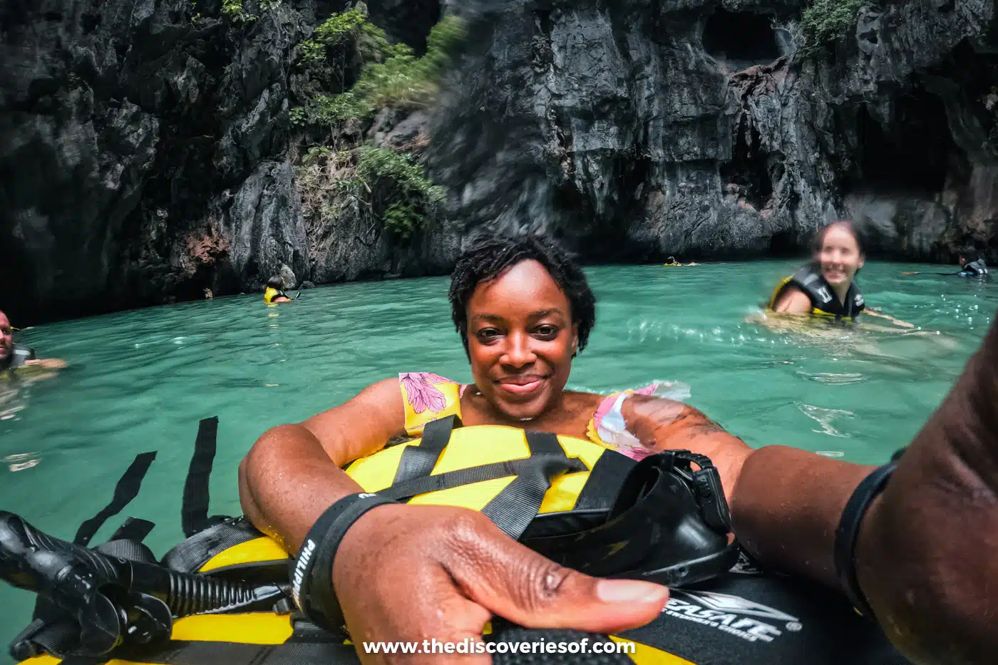 Julianna floating in a swim ring in a green lagoon below dark limestone cliffs on El Nido Tour A