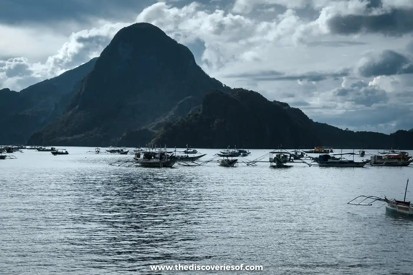 Bangka boats moored in the bay below the dark peak of Cadlao Island under a cloudy sky, El Nido
