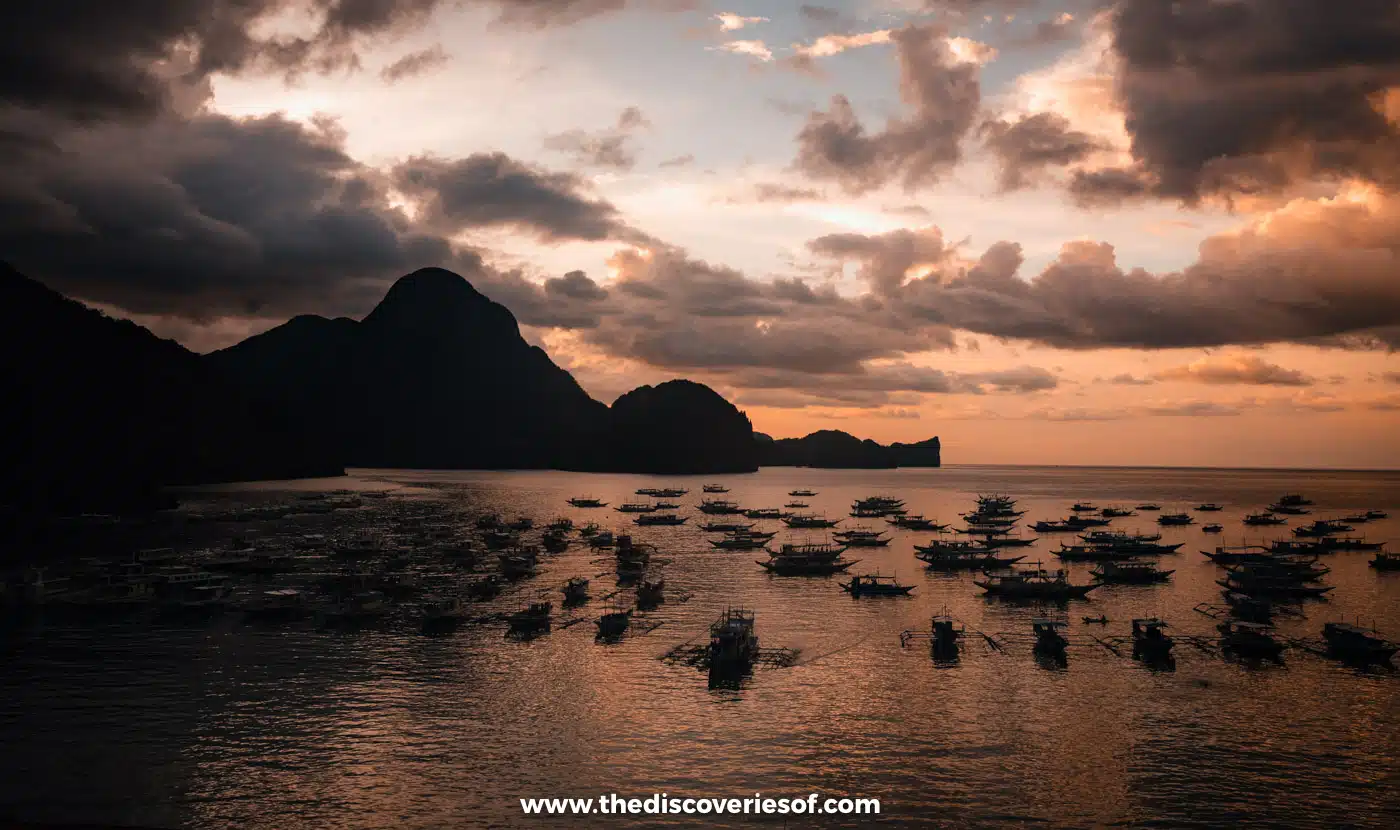 Silhouetted islands and moored boats under a dramatic orange sunset over Bacuit Bay, El Nido