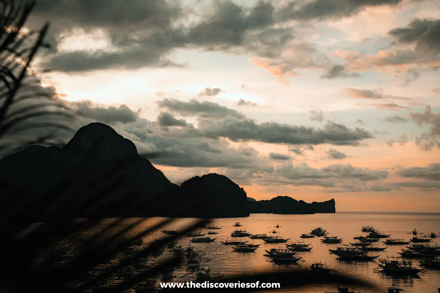 Silhouetted islands and moored boats under a cloudy orange sunset over Bacuit Bay, El Nido