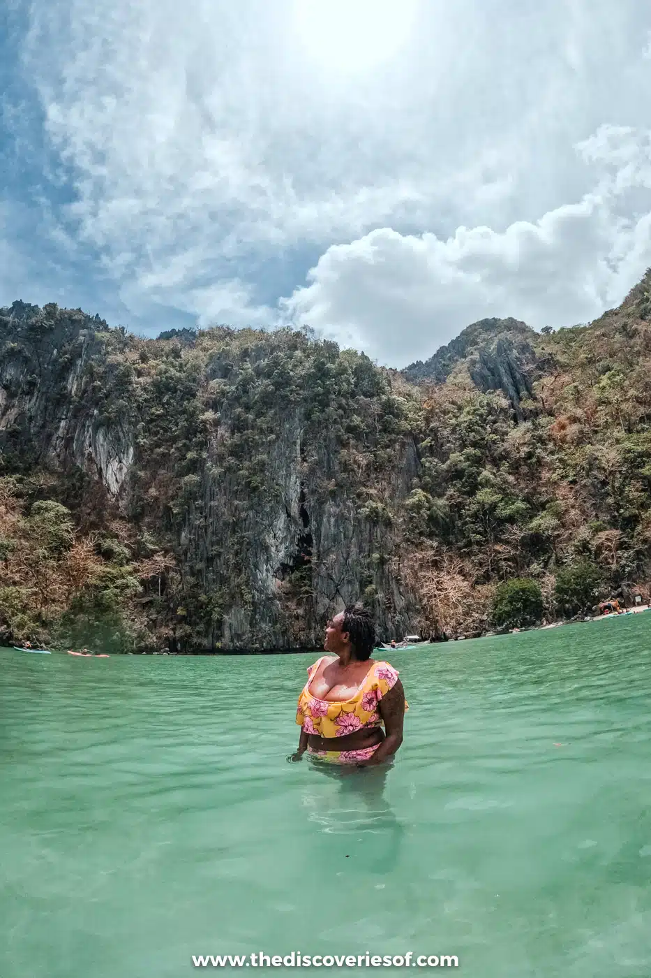Julianna standing waist-deep in the green water of Cadlao Lagoon below steep forested cliffs, El Nido