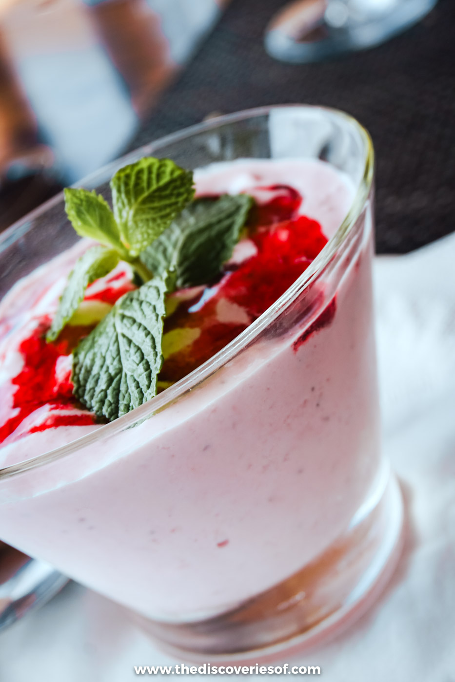 A glass of pale pink fruit mousse topped with berry sauce and a sprig of mint, a dessert at Estaminé