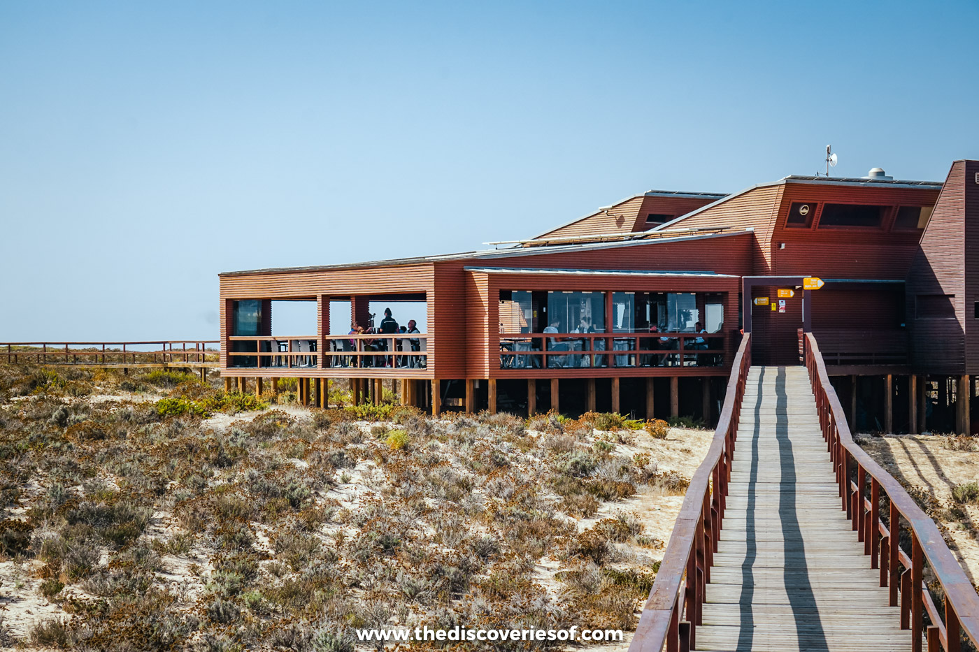 The wooden Estaminé restaurant raised on stilts above the dunes, with a railed boardwalk leading up to it, on Ilha Deserta
