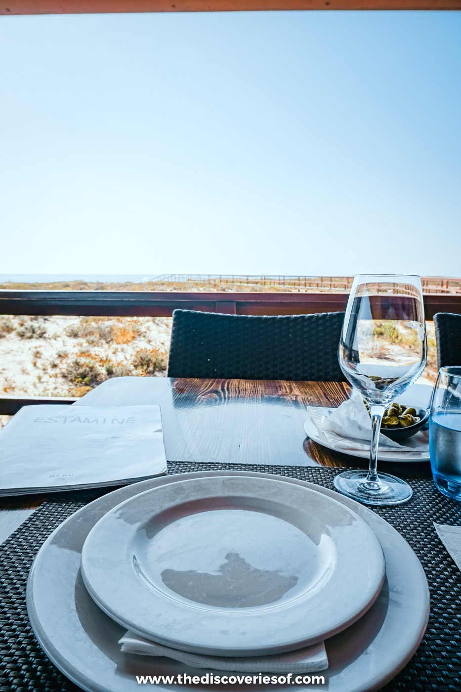 A laid table with plates and wine glasses on the terrace at Estaminé, overlooking the Ilha Deserta dunes