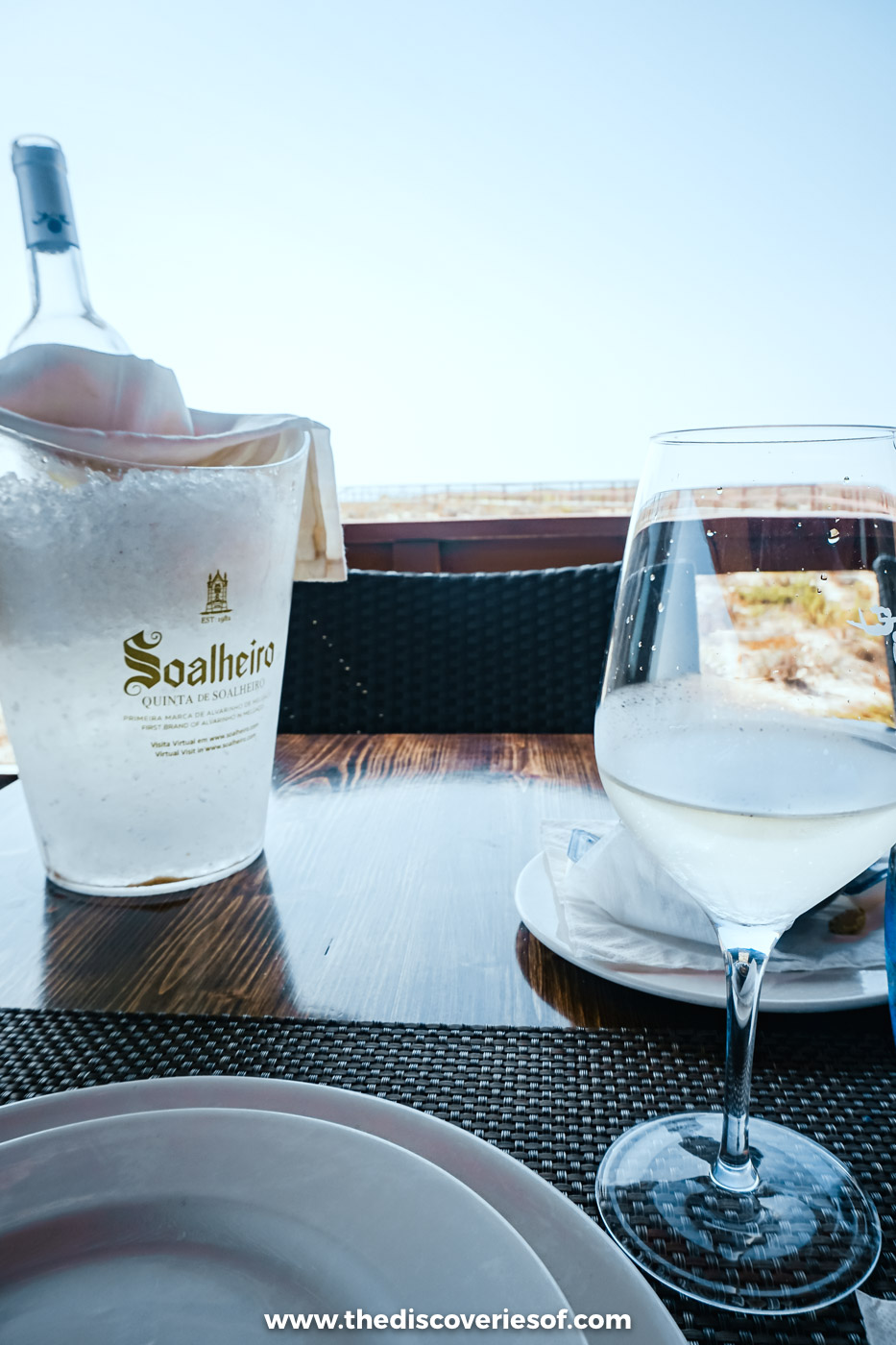 A bottle of white wine in an ice bucket and a filled glass on a table on the terrace of Estaminé on Ilha Deserta
