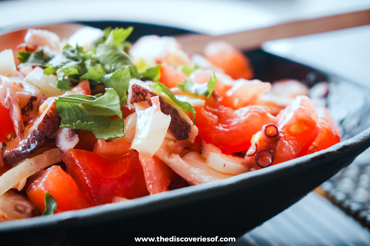 An Algarve octopus salad with tomato, onion and fresh herbs in a dark bowl at Estaminé on Ilha Deserta