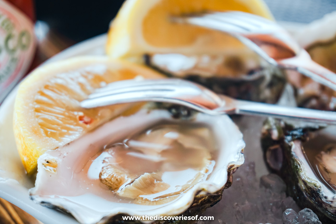Close-up of a fresh Ria Formosa oyster with lemon wedges and a fork at Estaminé on Ilha Deserta