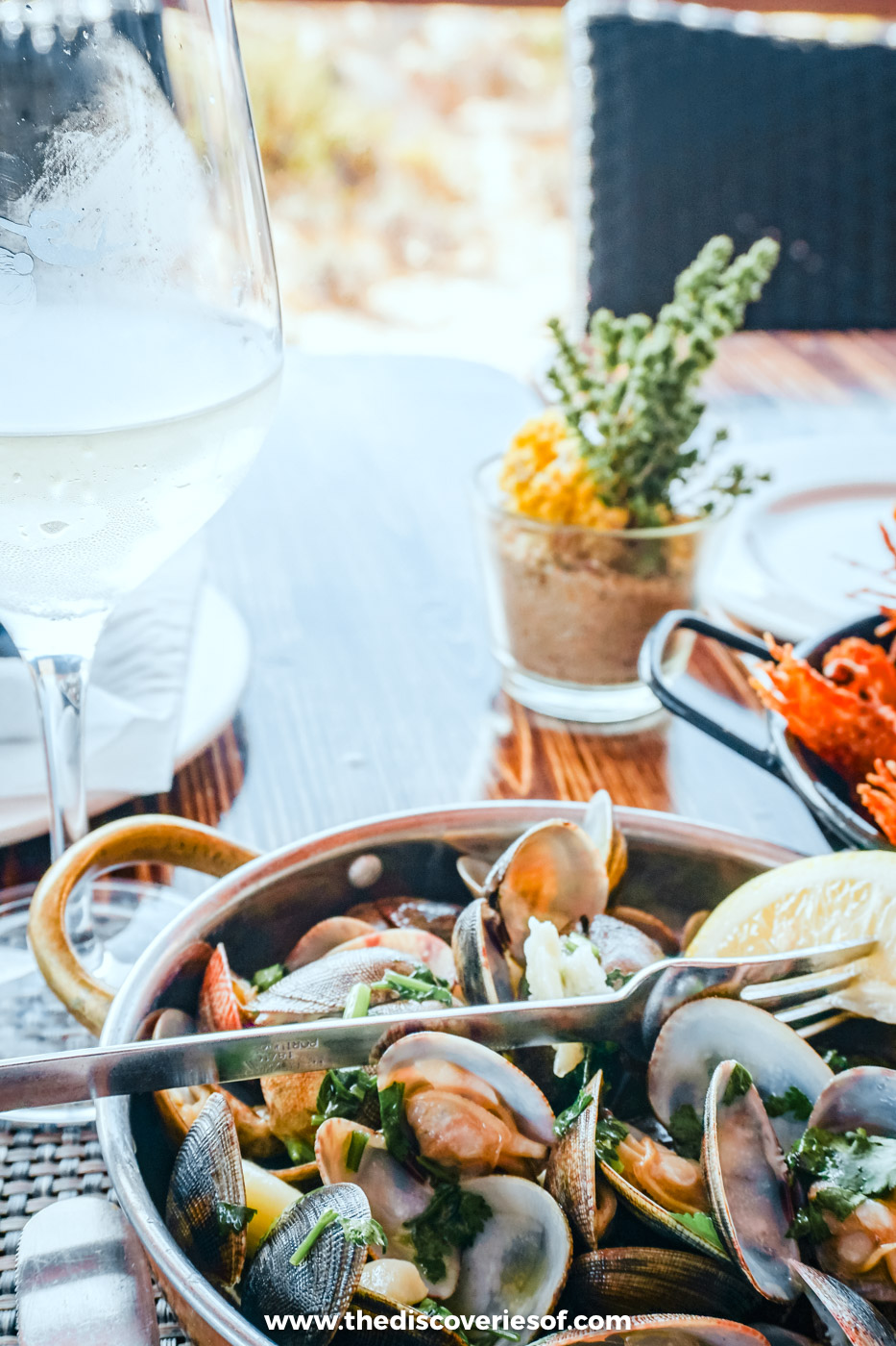 A pan of clams with coriander and lemon beside a glass of white wine at Estaminé on Ilha Deserta