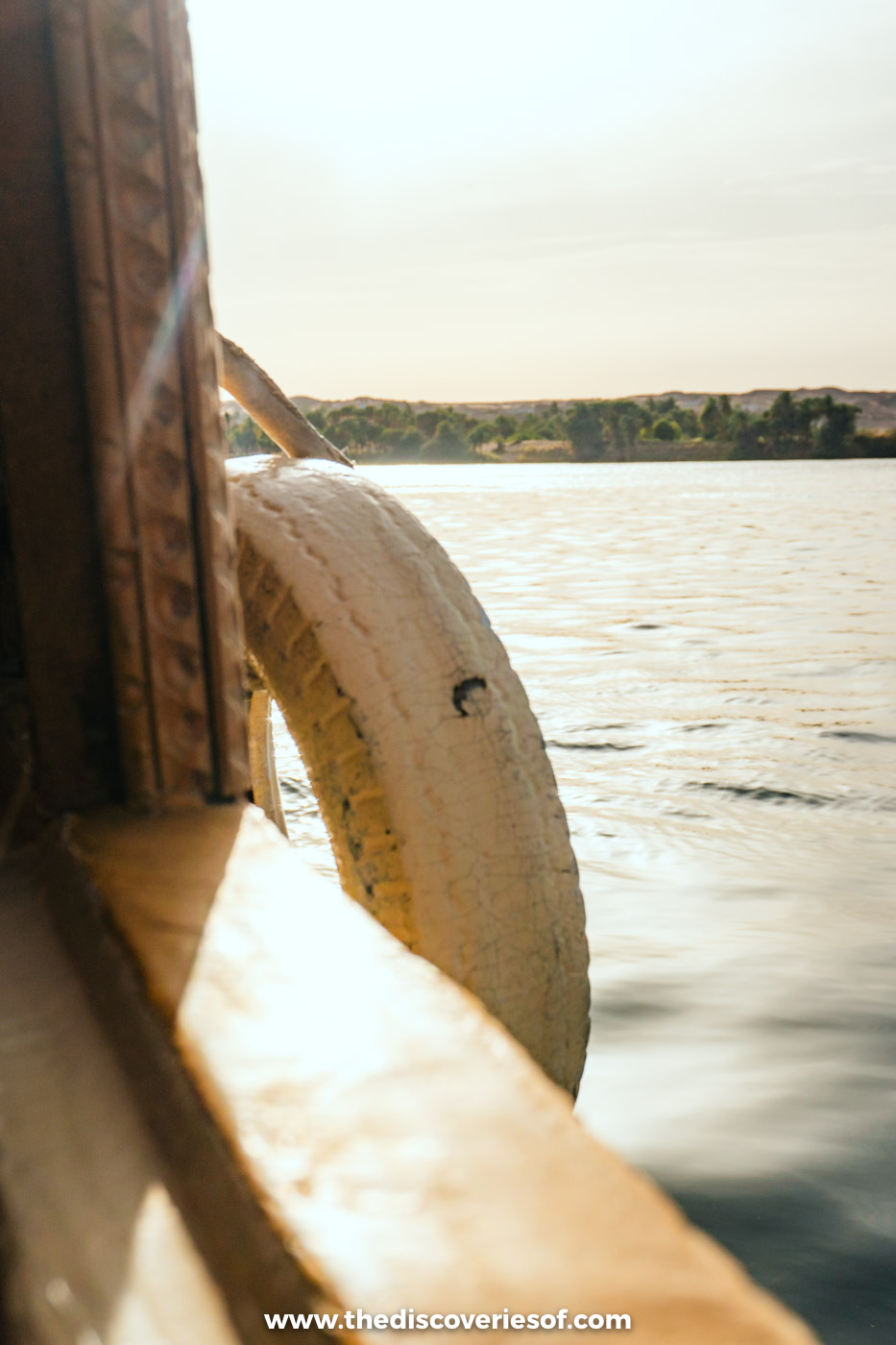 A white fender hanging from the wooden side of a felucca as it glides along the sunlit Nile