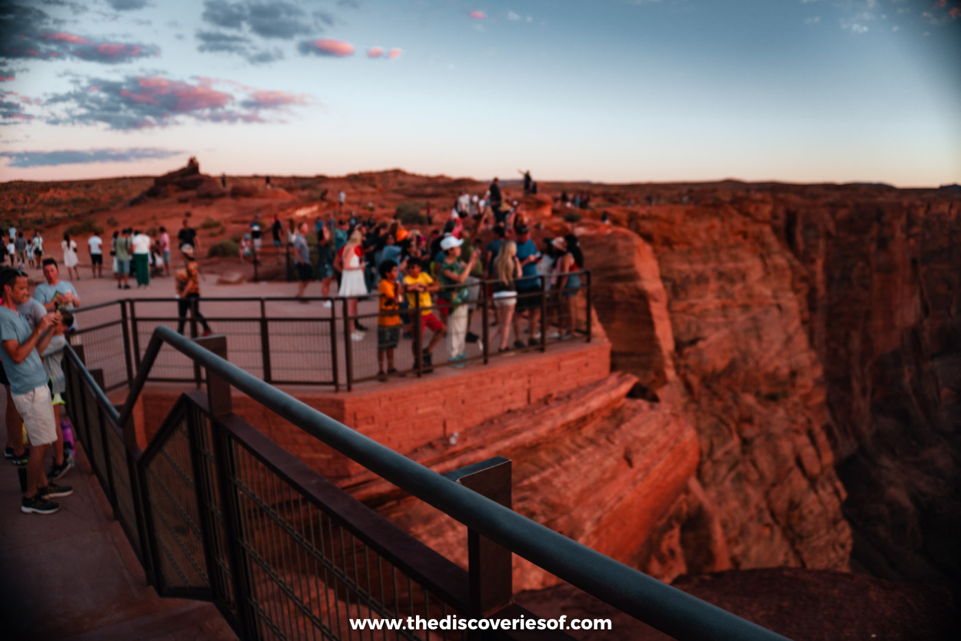Crowds lining the railing at the Horseshoe Bend overlook at sunset