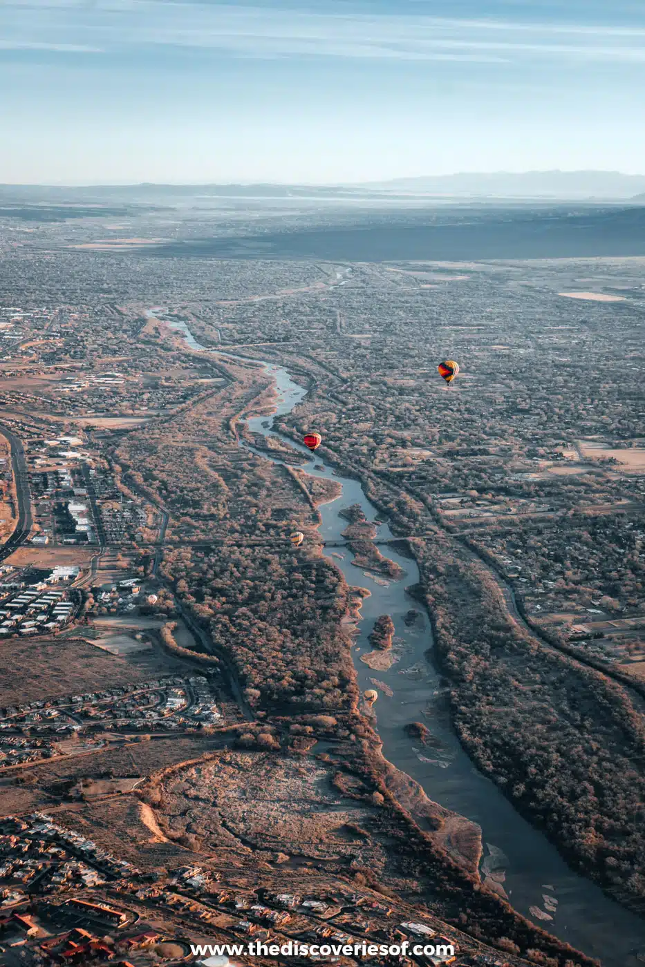 Aerial view of the Rio Grande winding through the cottonwood bosque in Albuquerque, with hot air balloons in the distance