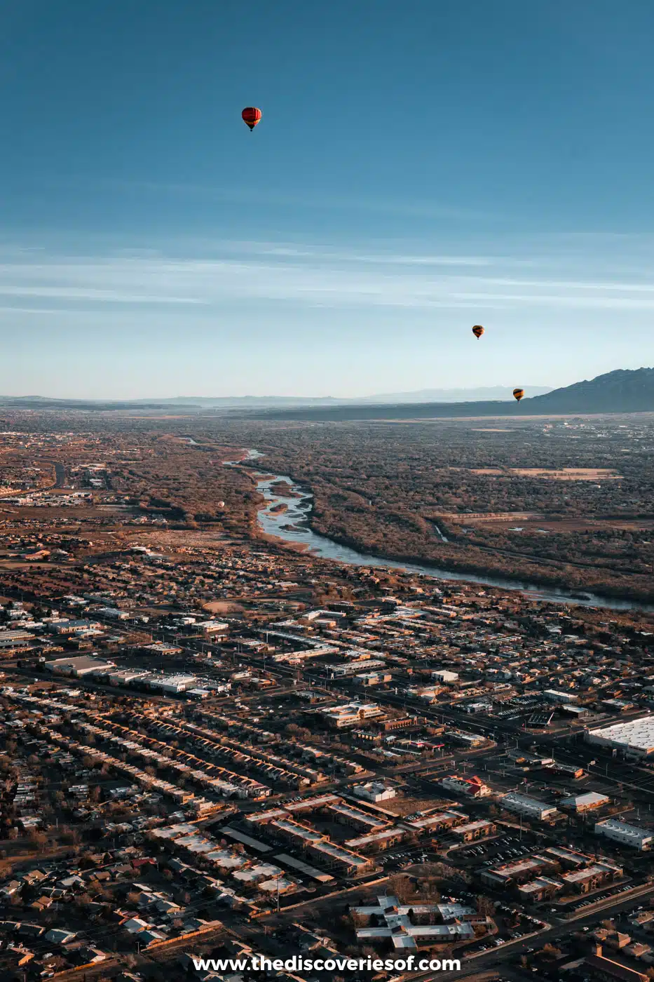 Three hot air balloons drifting high above the Rio Grande and the city of Albuquerque with the Sandia Mountains behind