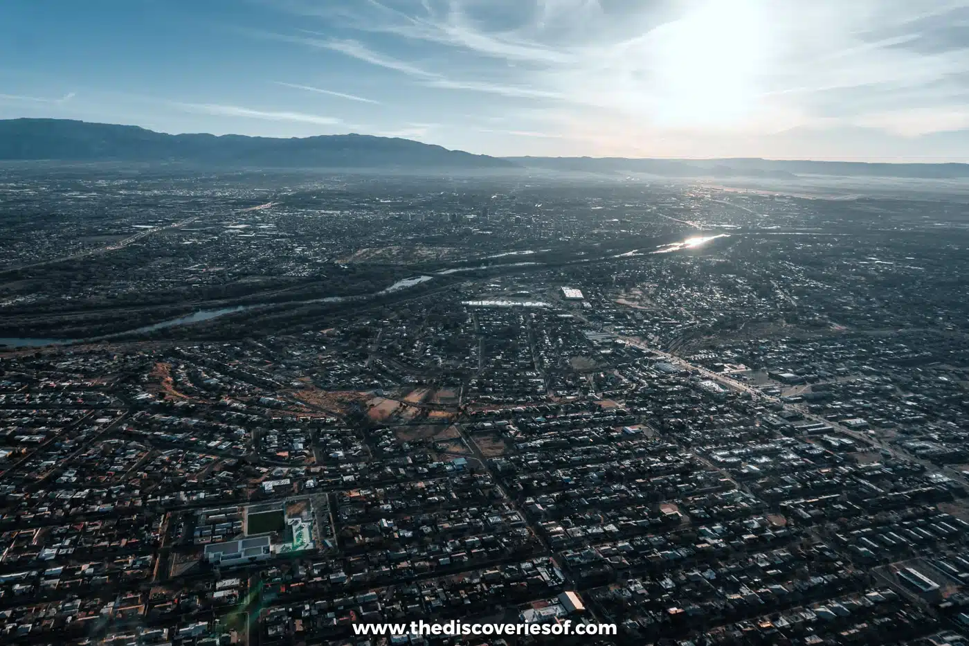 Albuquerque's streets and rooftops stretching to the mountains, seen from a hot air balloon at sunrise