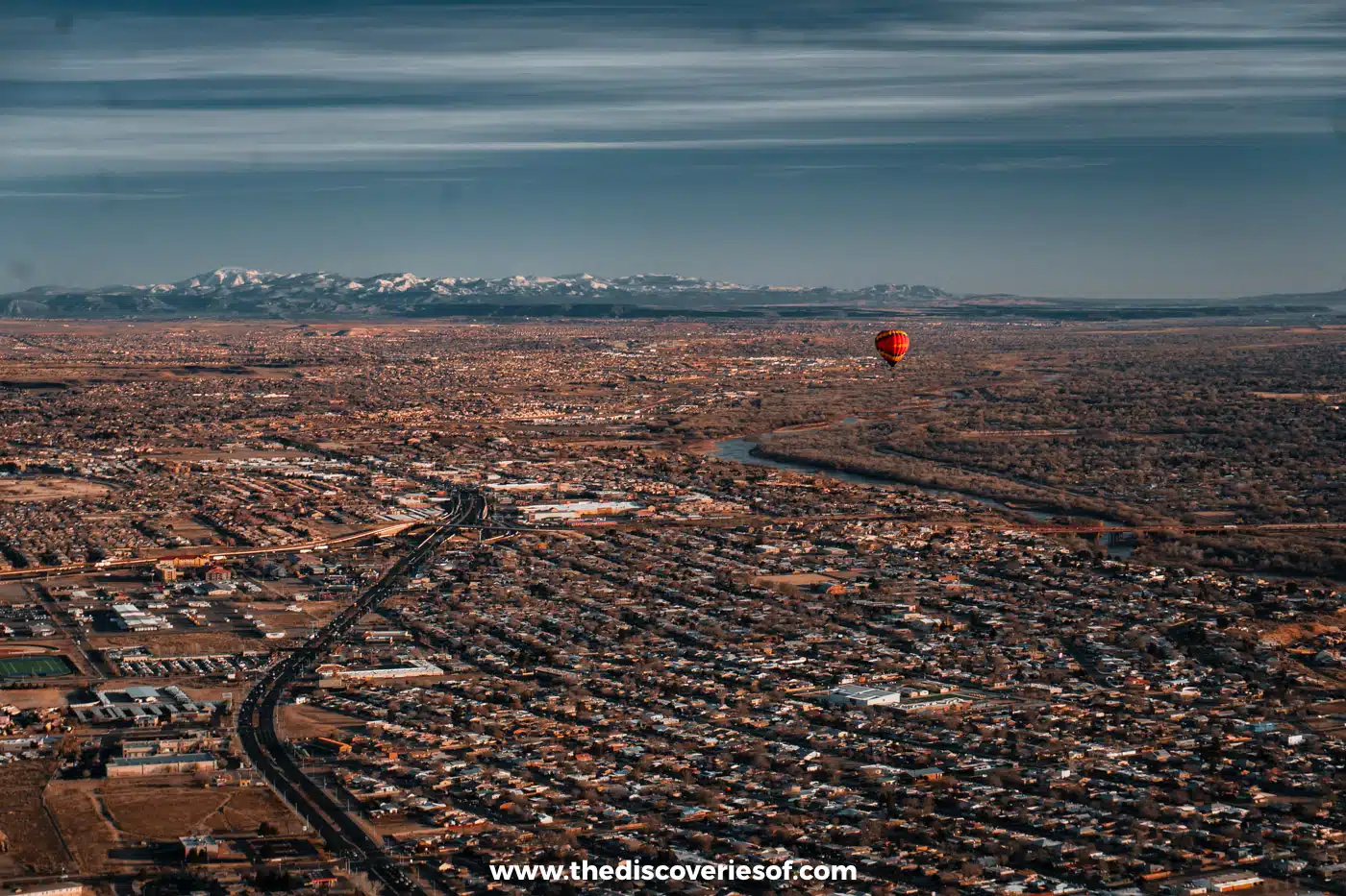 Albuquerque stretching towards snow-capped mountains, seen from a hot air balloon with another balloon nearby
