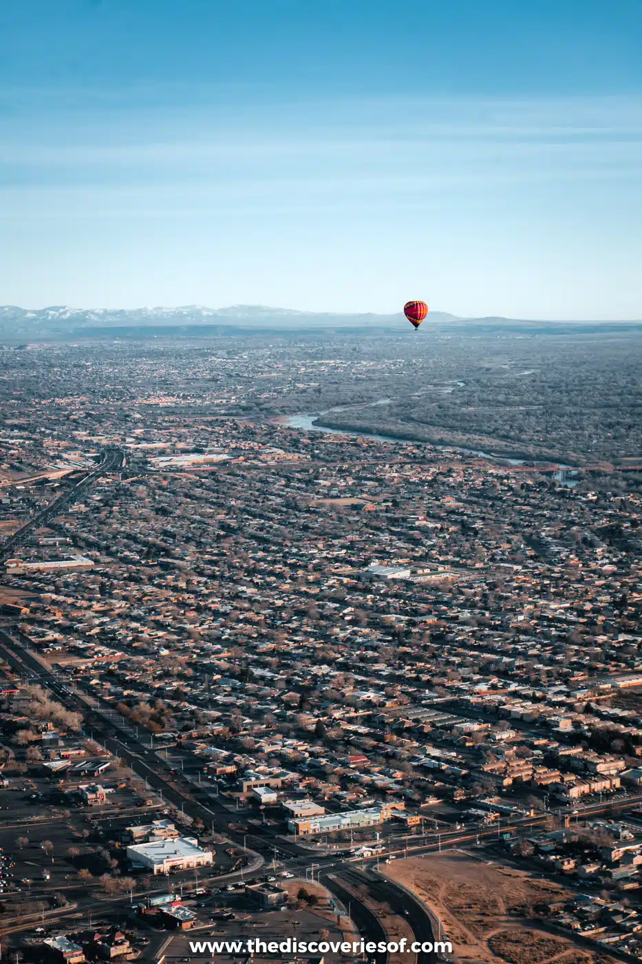 Red hot air balloon floating above the streets and rooftops of Albuquerque with the mountains on the horizon