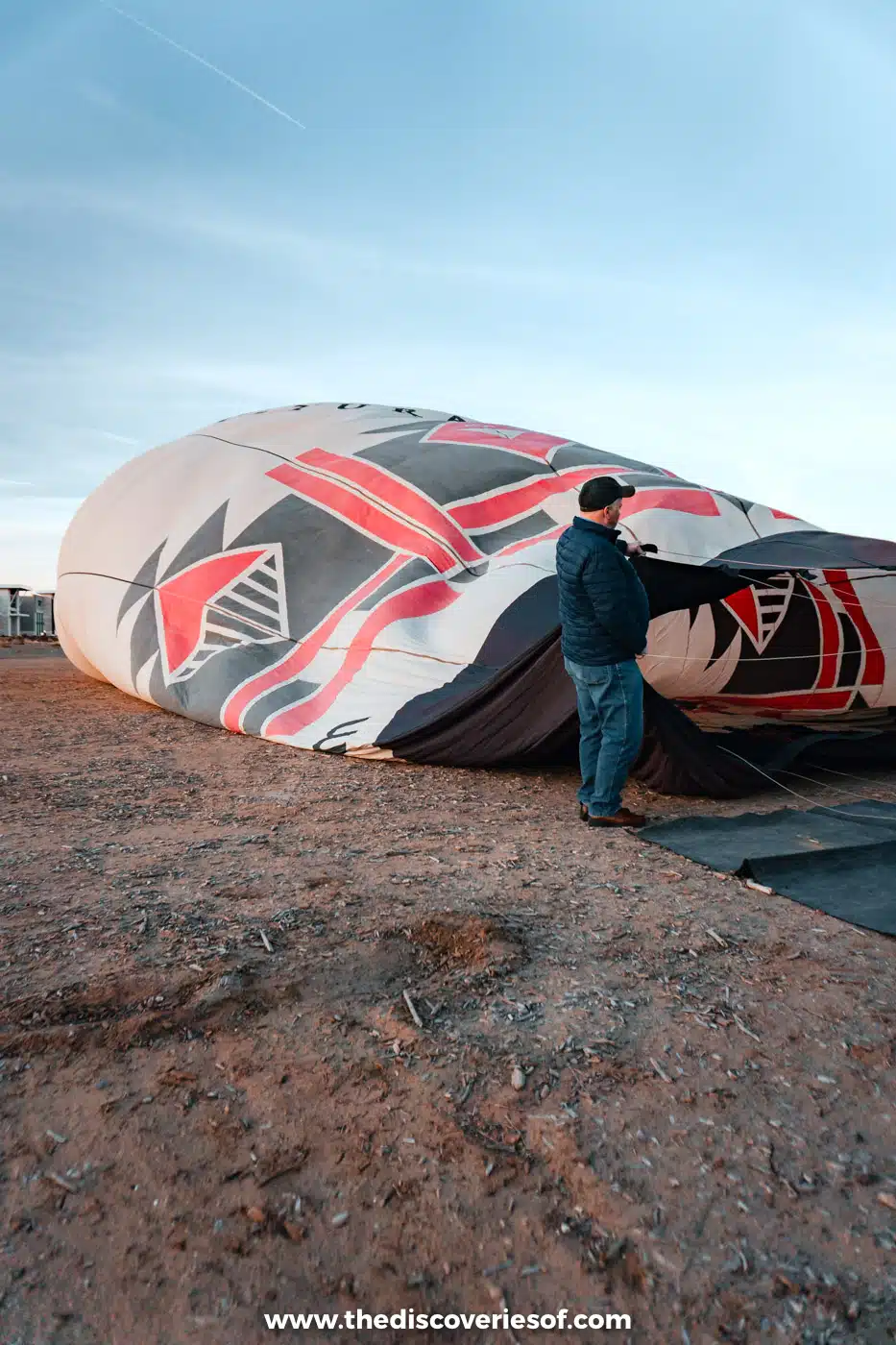 Crew member deflating and packing away a patterned hot air balloon on open ground after landing in Albuquerque