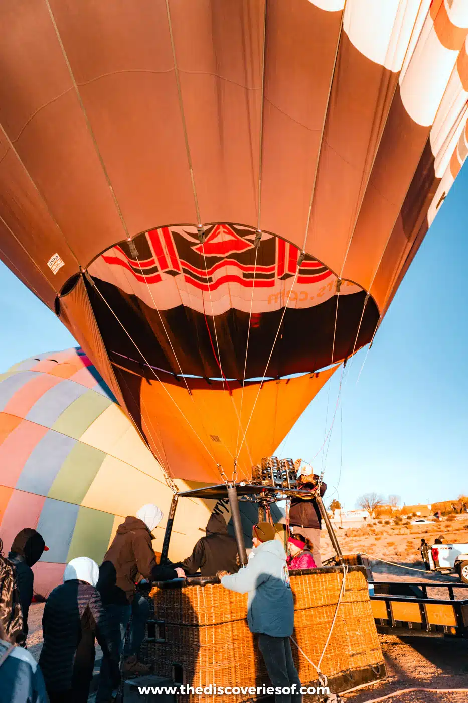 Orange hot air balloon standing upright over its basket as passengers gather at a launch site in Albuquerque