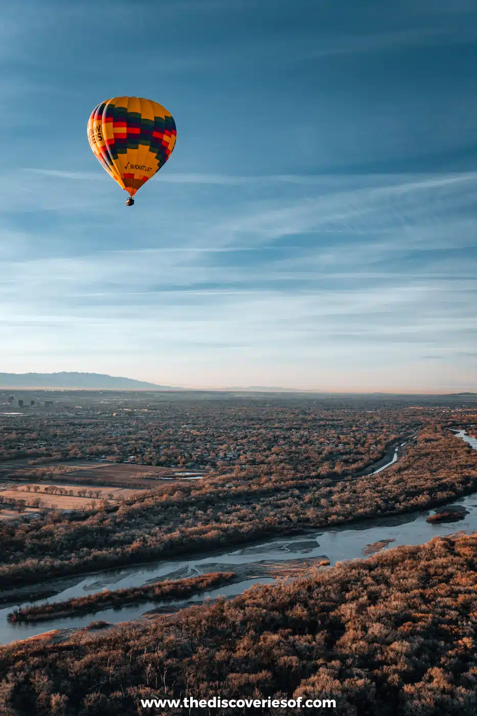 Colourful striped hot air balloon floating above the Rio Grande and its cottonwood bosque in Albuquerque