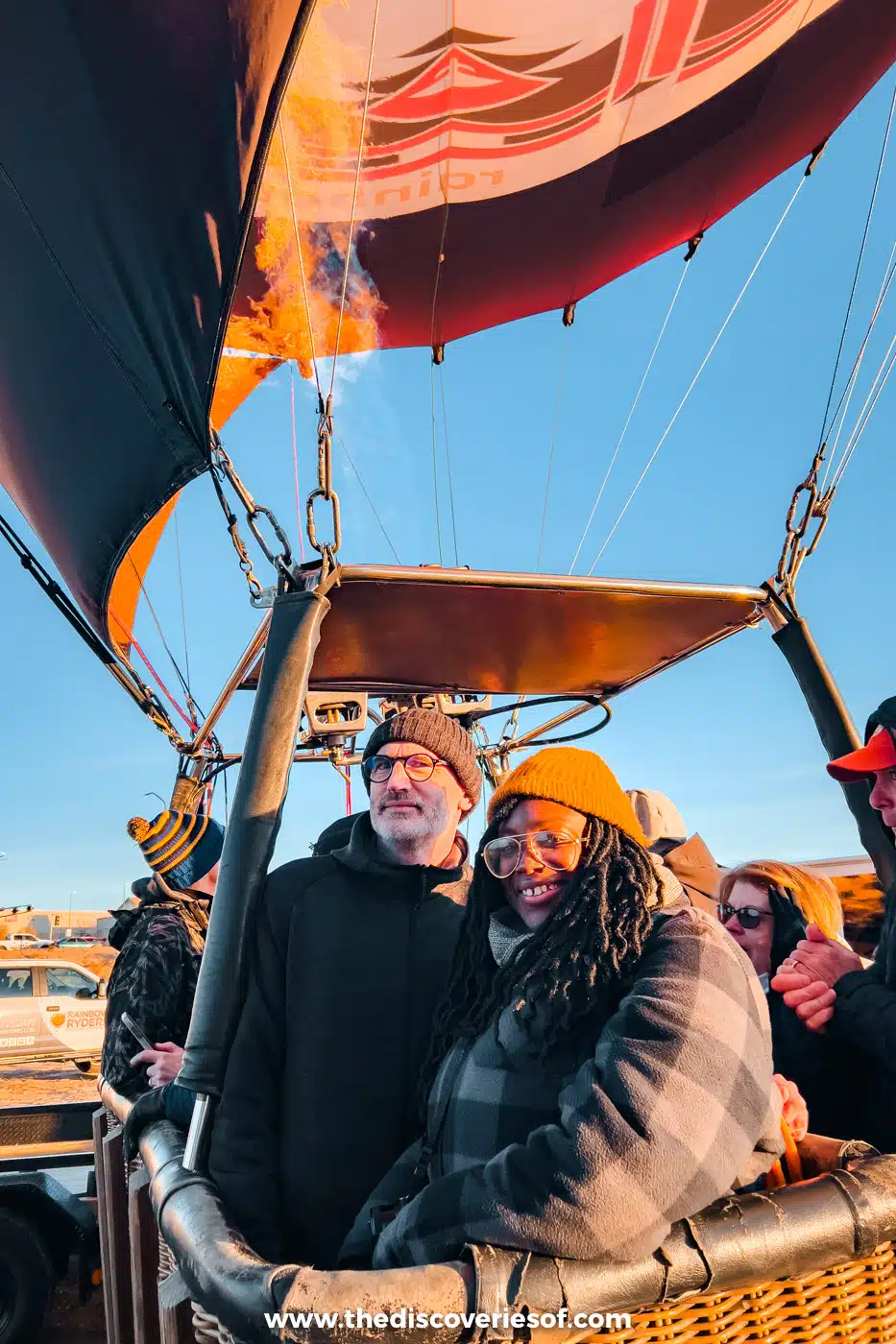 Julianna smiling in a hot air balloon basket under the lit burner before a sunrise flight in Albuquerque