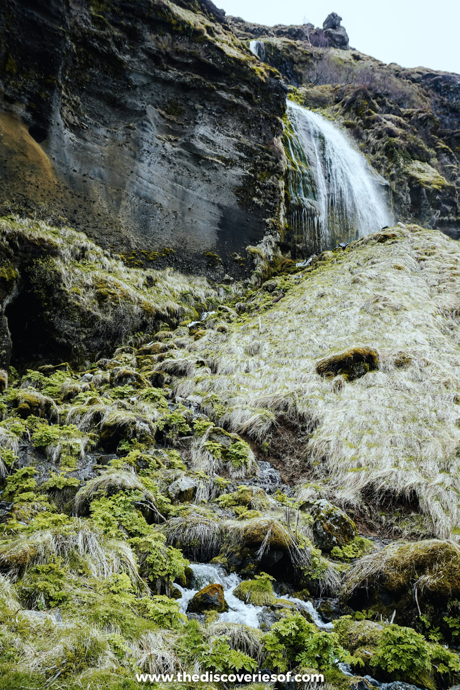 A small waterfall spilling down a mossy cliff above pale winter grass on the walk from Seljalandsfoss to Gljúfrabúi