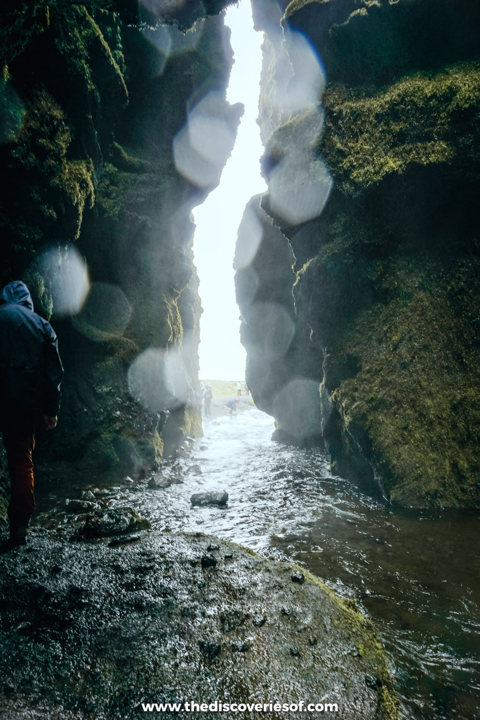 A visitor walking out of the narrow slit into Gljúfrabúi gorge as the stream runs over rocks towards daylight