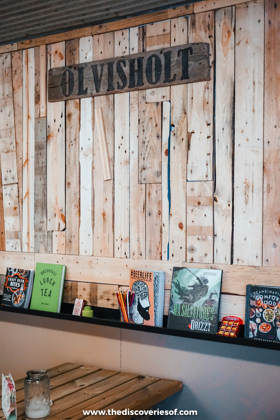 Ölvisholt name sign on a reclaimed wood wall above a shelf of beer bottles at the brewery