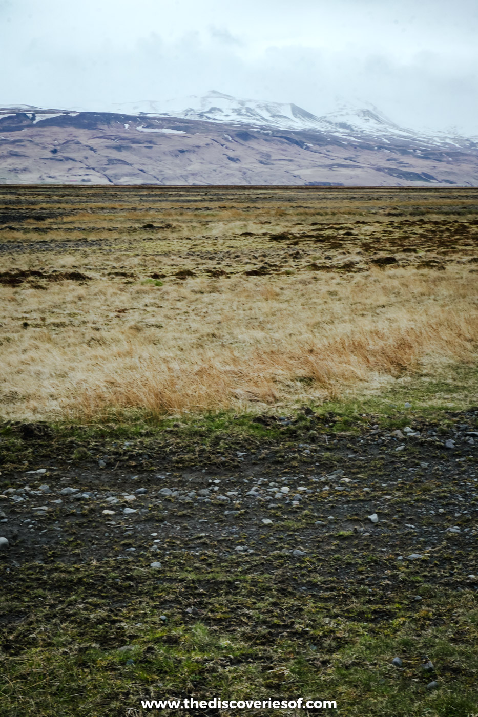 Straw-coloured grassland below a snow-capped mountain under a grey sky on the super jeep route towards Þórsmörk