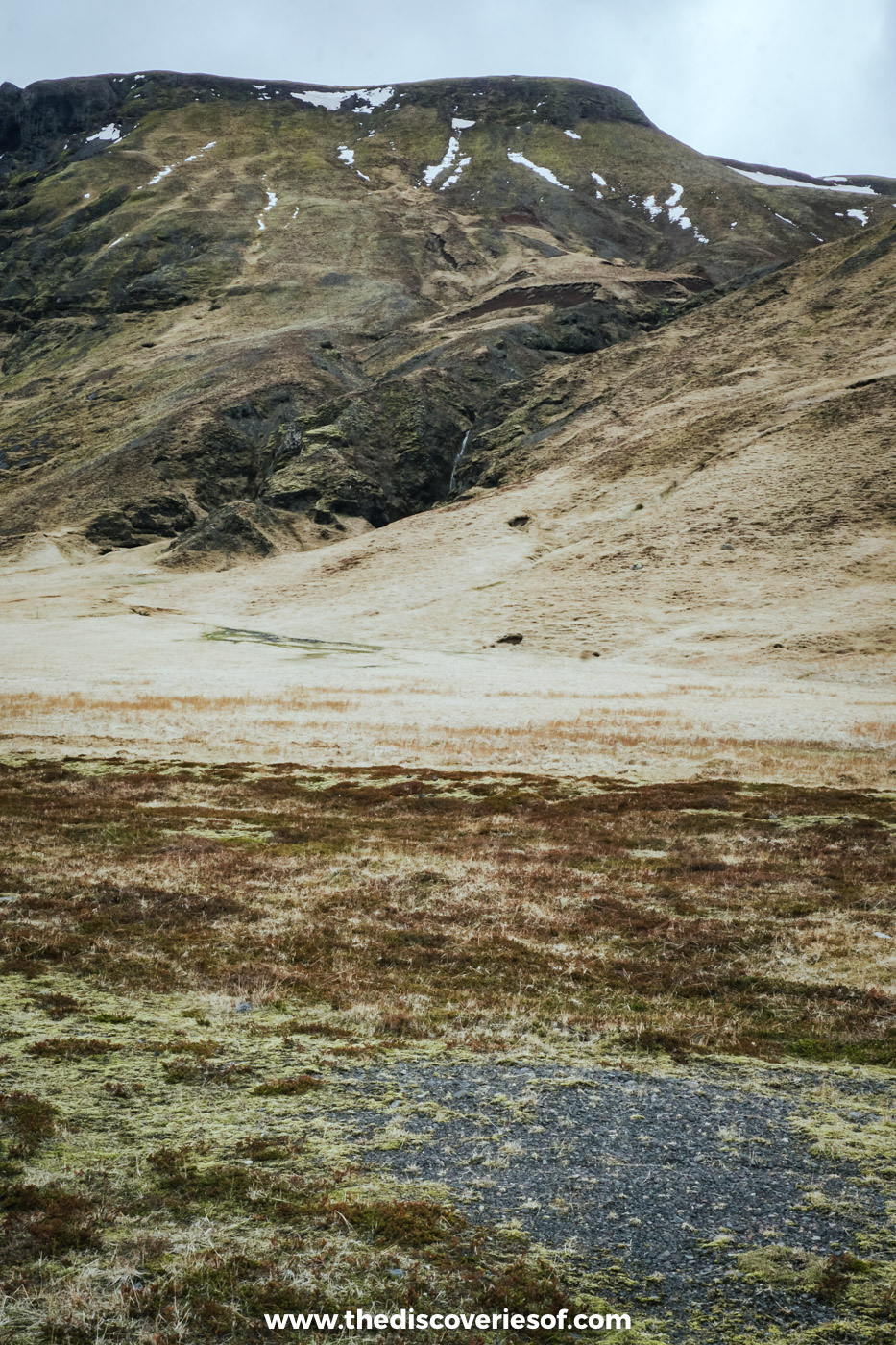 Brown hillside streaked with old snow above pale grassland on a super jeep route in south Iceland